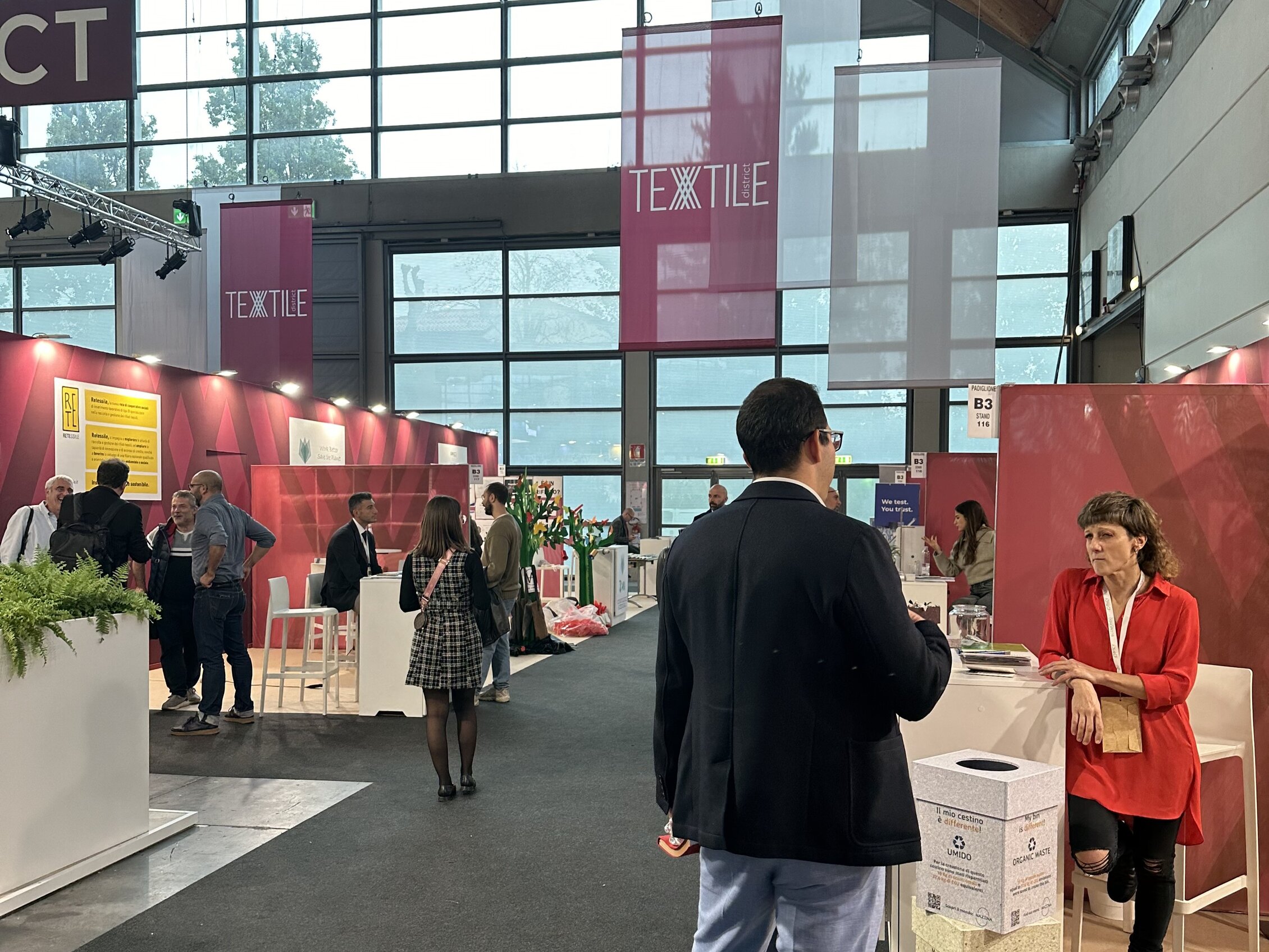 Visitatori interagiscono con gli espositori all'interno dell'area 'TEXTILE' circondati da stand colorati e decorazioni moderne