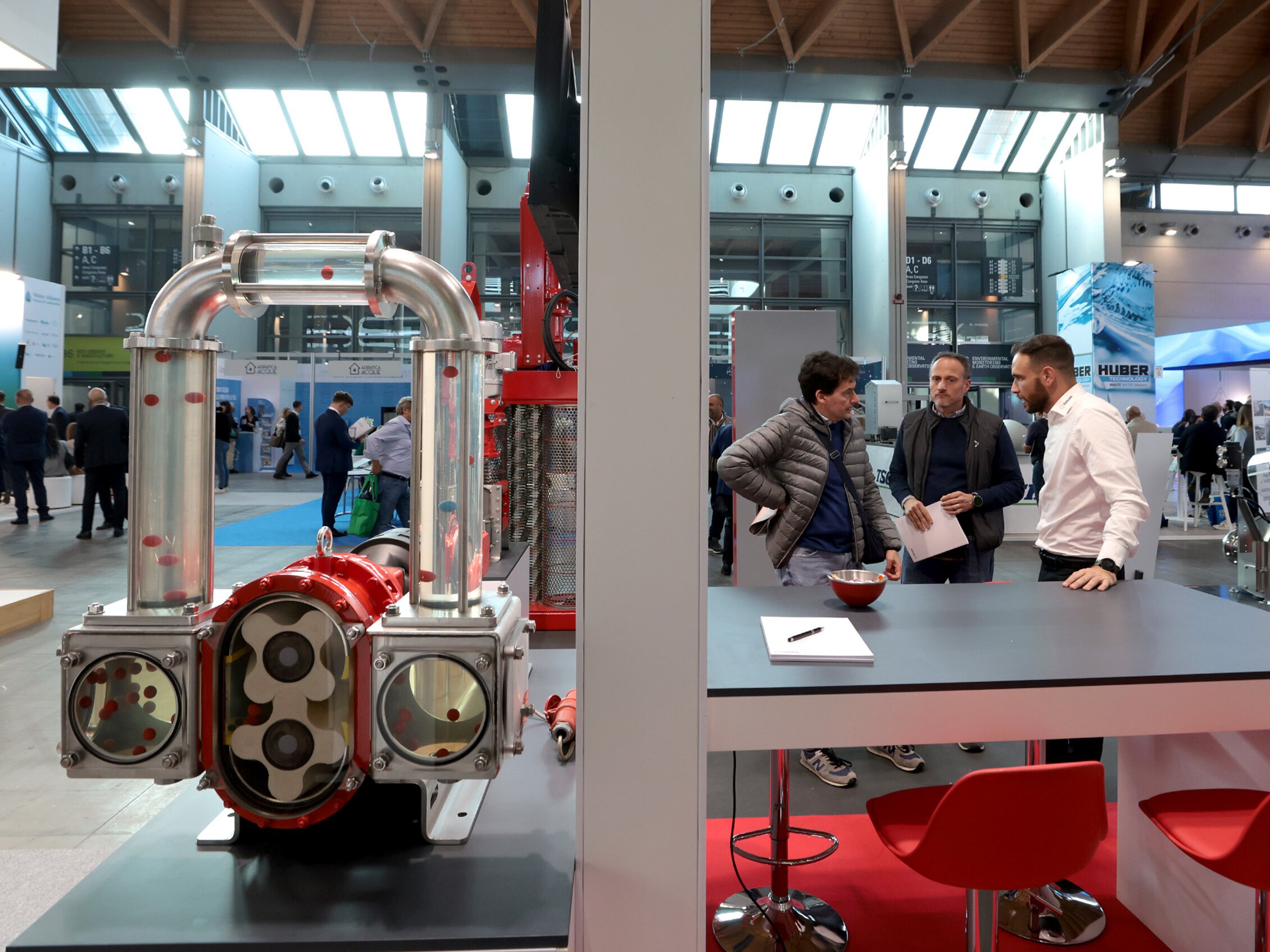 tre partecipanti a Ecomondo dialogano accanto a un’innovativa pompa a lobi rotativi della Vogelsang, esposta nello stand della fiera