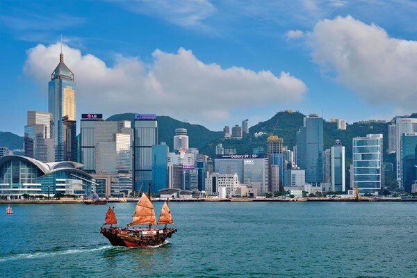 una barca a vela in legno naviga di fronte al moderno skyline di hong kong