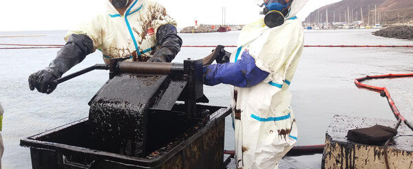 due agenti sanitari lavorano per limitare i danni di una fuoriuscita di petrolio in mare