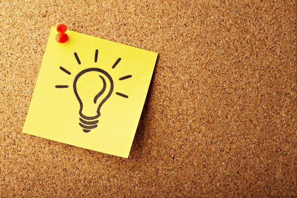 a post-it note hanging on a notice board depicting a stylised icon of a light bulb on
