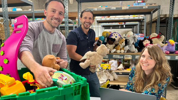  three smiling people inside a warehouse sorting children's toys for reuse