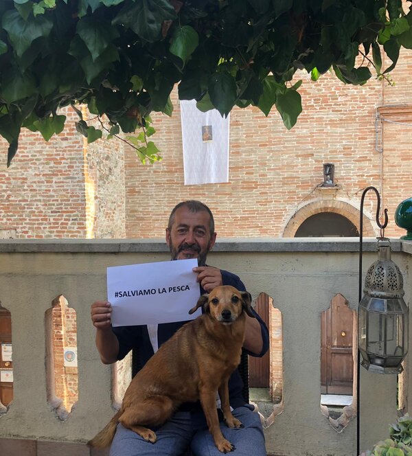 massimo bellavista con un cane in braccio tiene in mano un cartello con su scritto salviamo la pesca