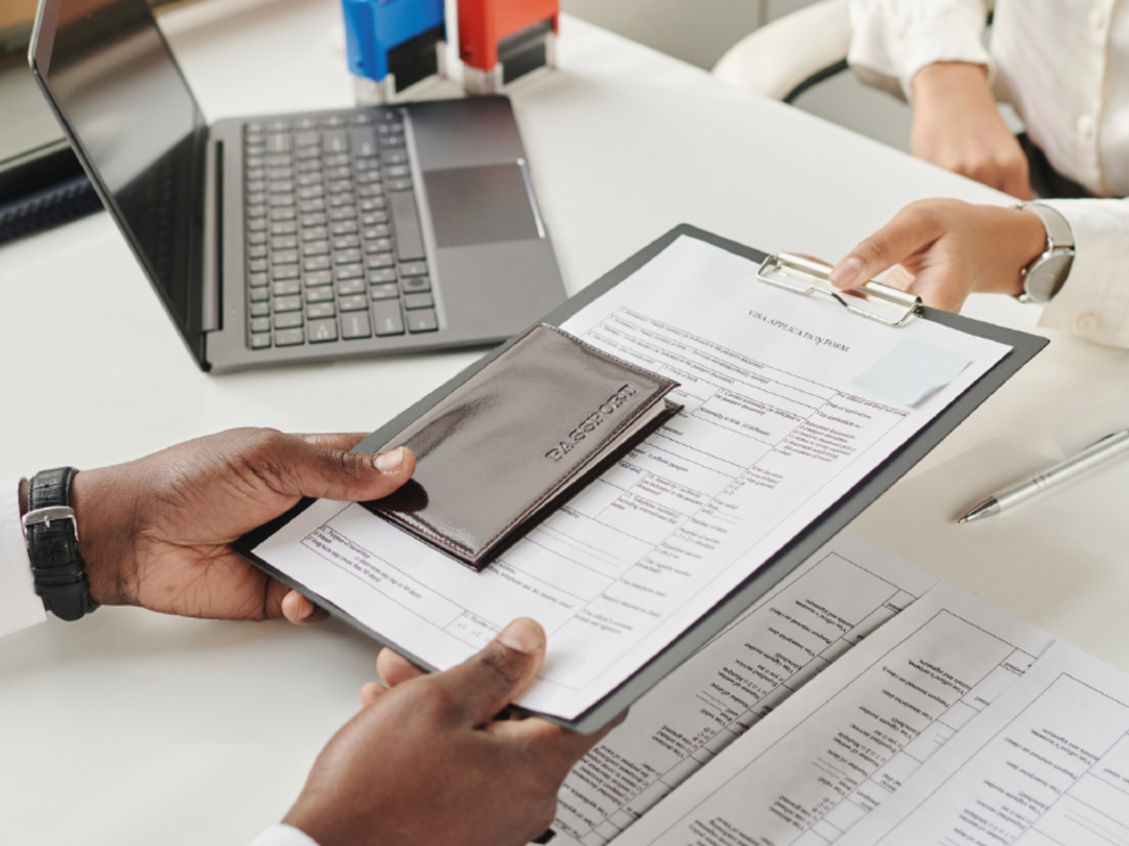 At the desk, someone hands over a passport and visa documents to an individual sitting across